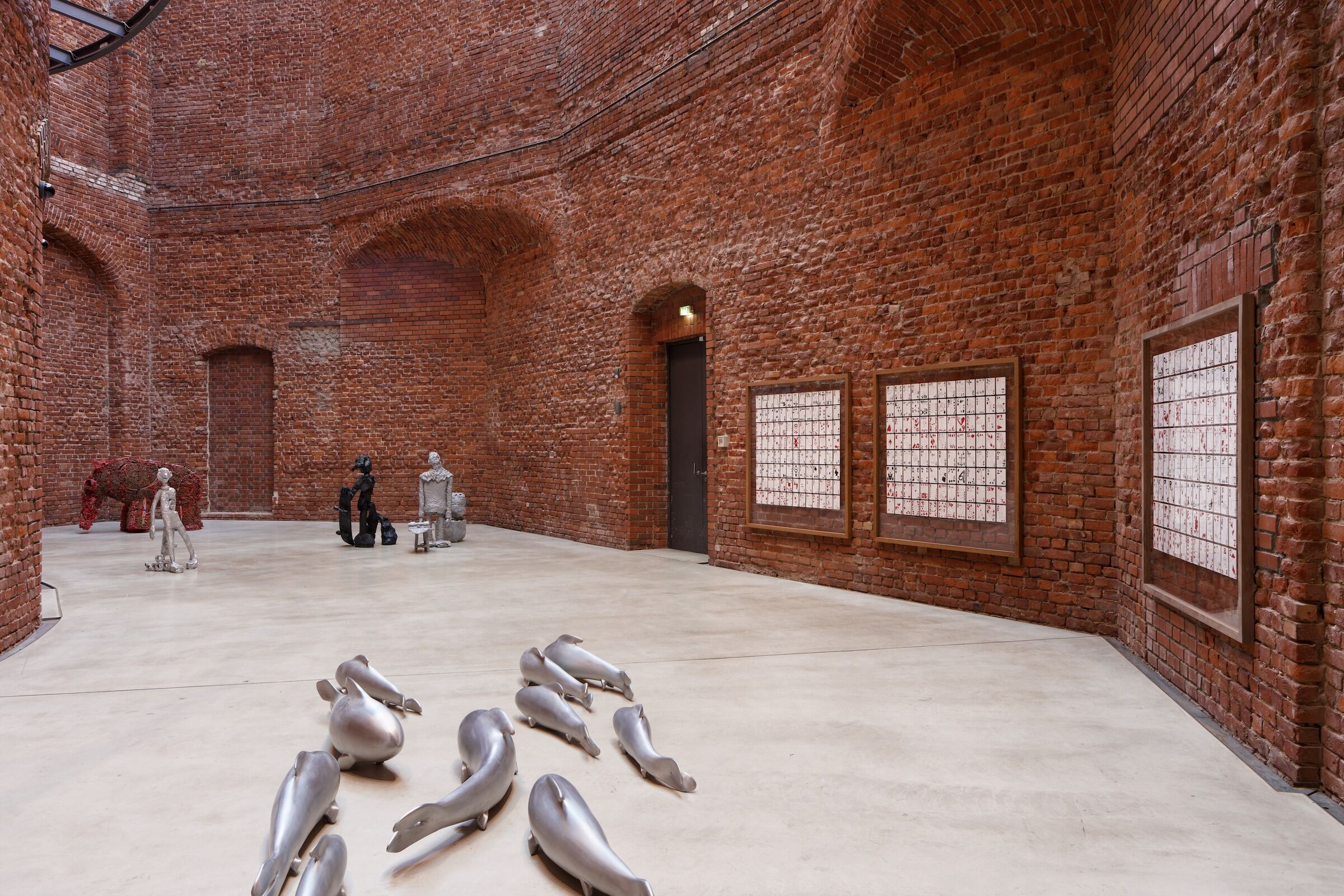 Bronze und Aluskulpturen in einem roten Backsteinraum. Wandarbeit: gemalte Spielkarten in Rahmen.