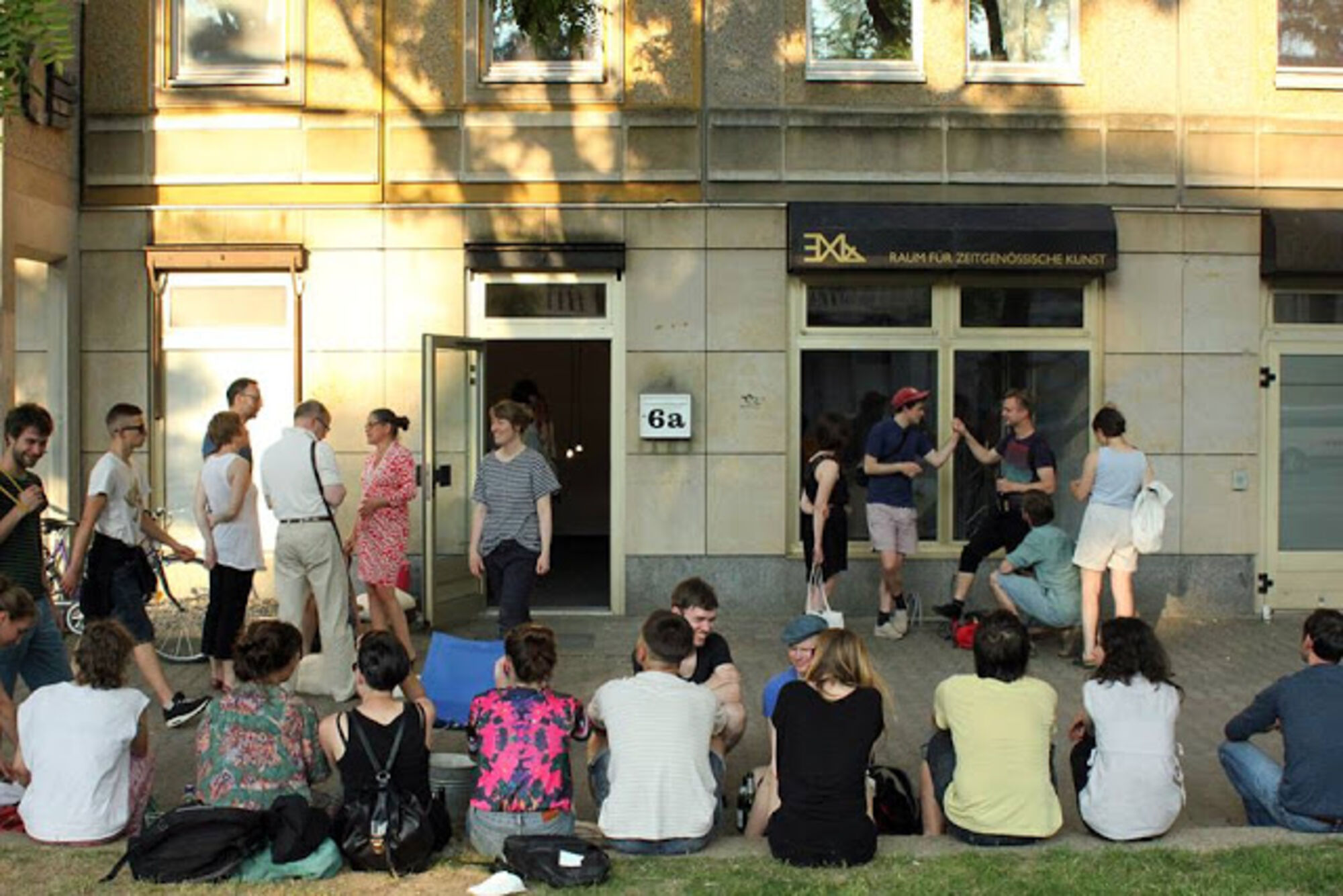 Menschen sitzen und unterhalten sich vor der Galerie EX14.