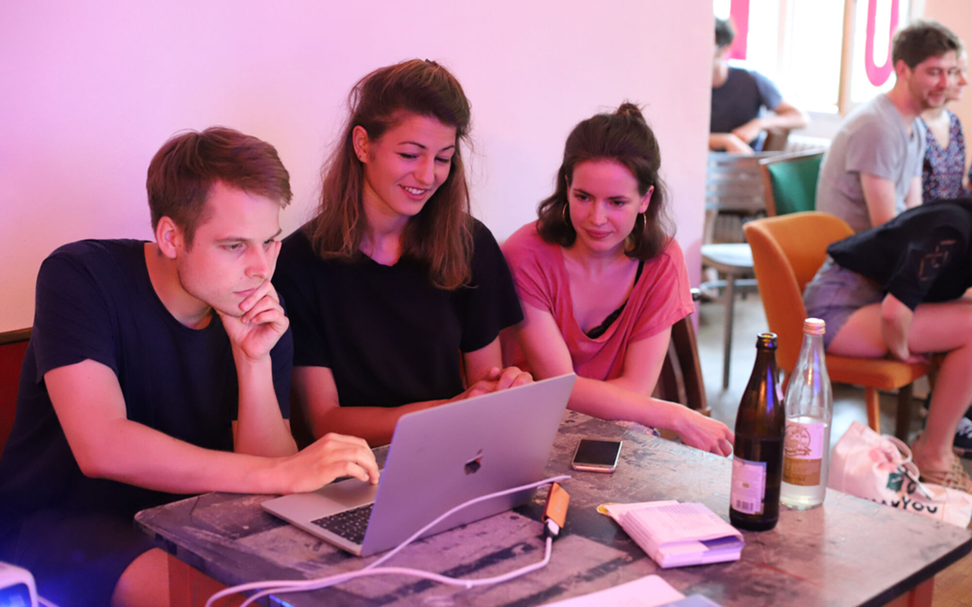 Ein Man und zwei Frauen sitzen am Tisch und gucken Videos auf einem Laptop-Computer.