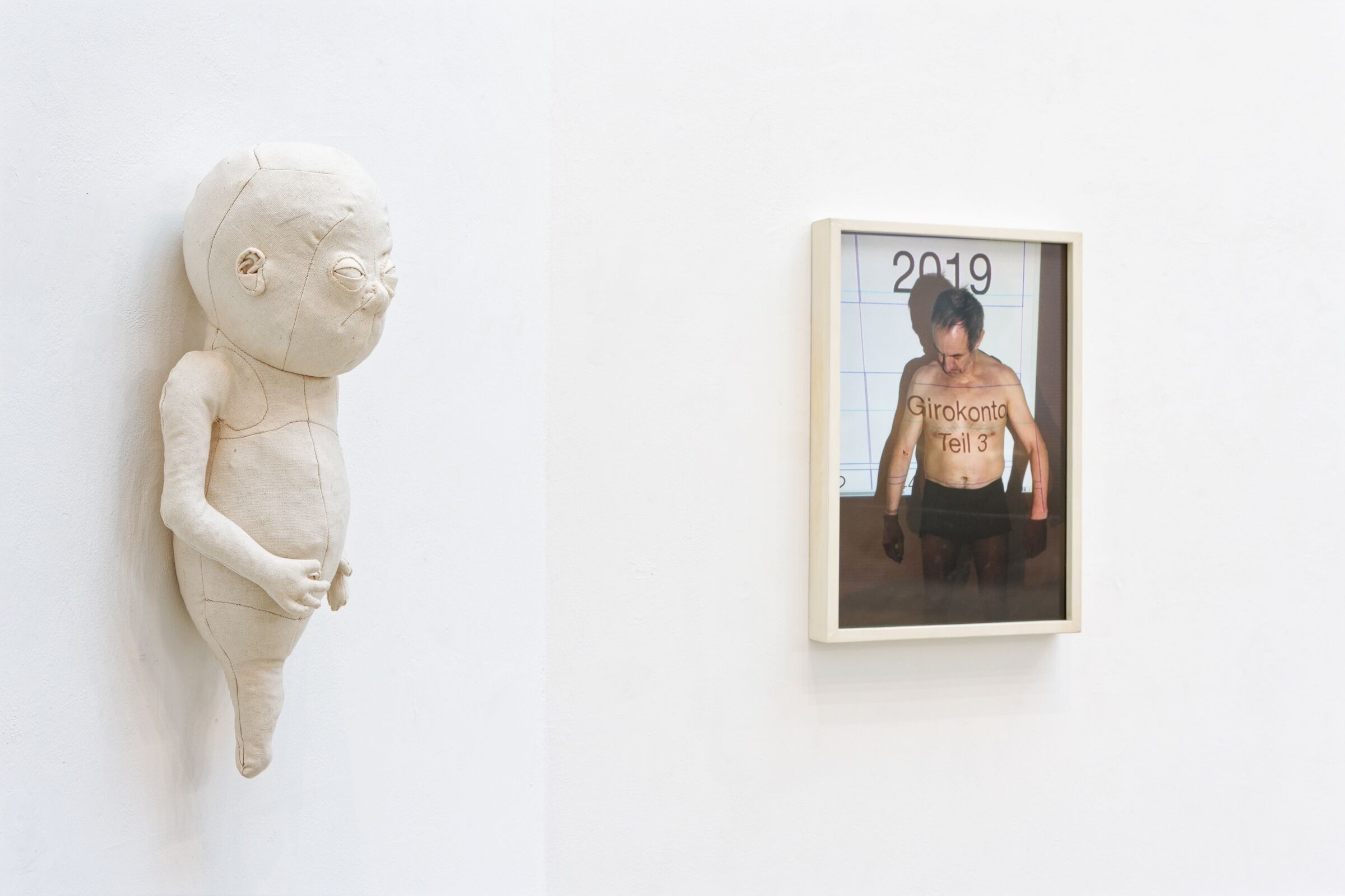 Textilarbeit und Foto des Künstlers mit nacktem Oberkörper an Wand.