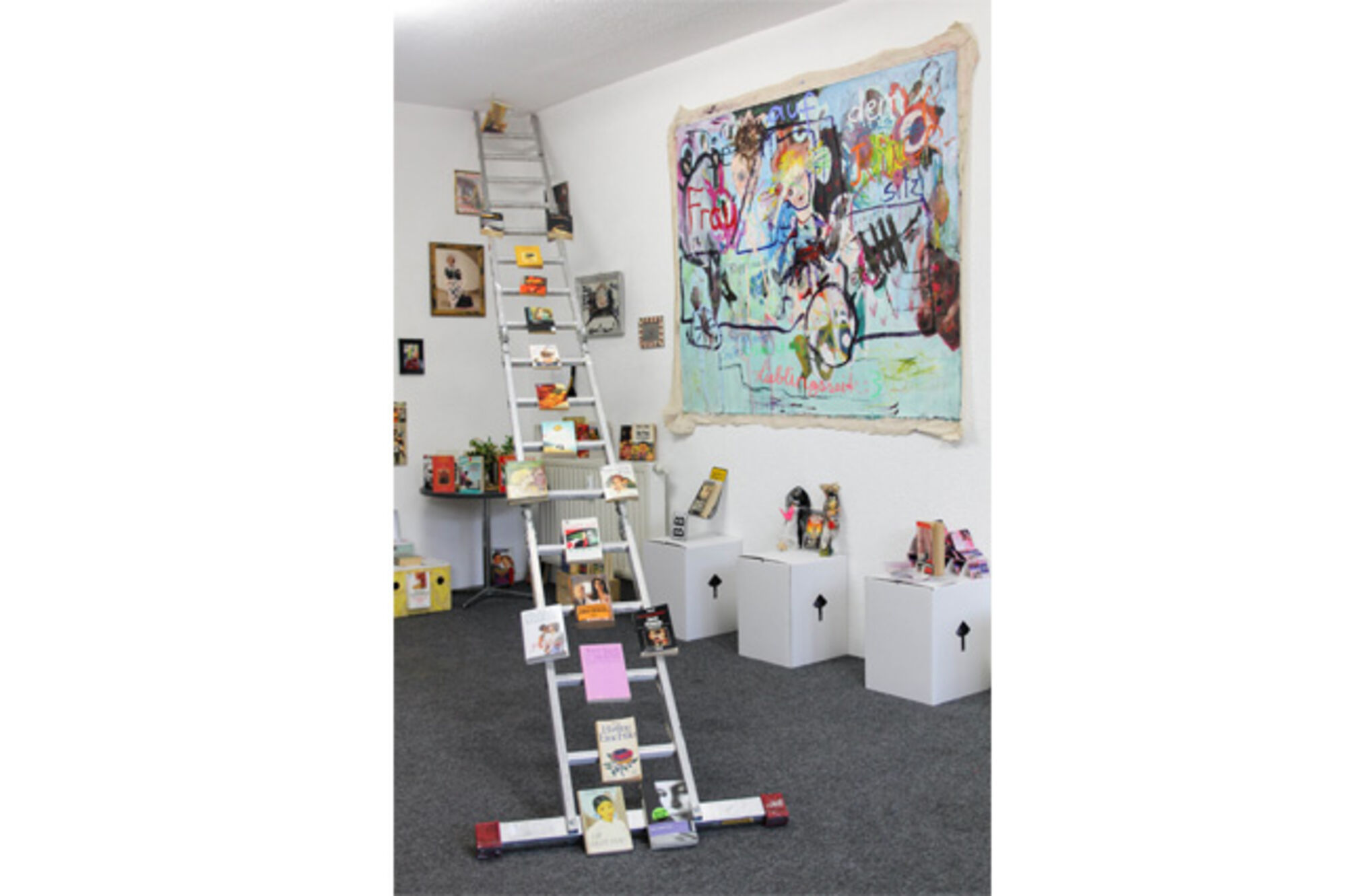 Installation in der Galerie EX14. Verschiedene Objekte im Raum: Leiter, Fotos, großes Gemälde und Ähnliches.