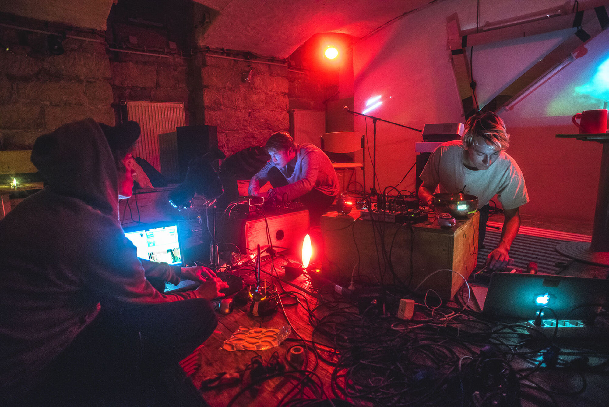 Drei DJs spielen Musik-Mixer im Raum. Den Raum ist mit roten LED-Leuchten belichtet.