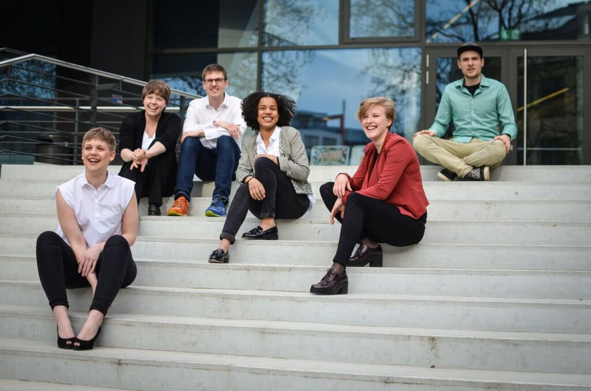 Sechs lachende Menschen sitzen an der Treppe.