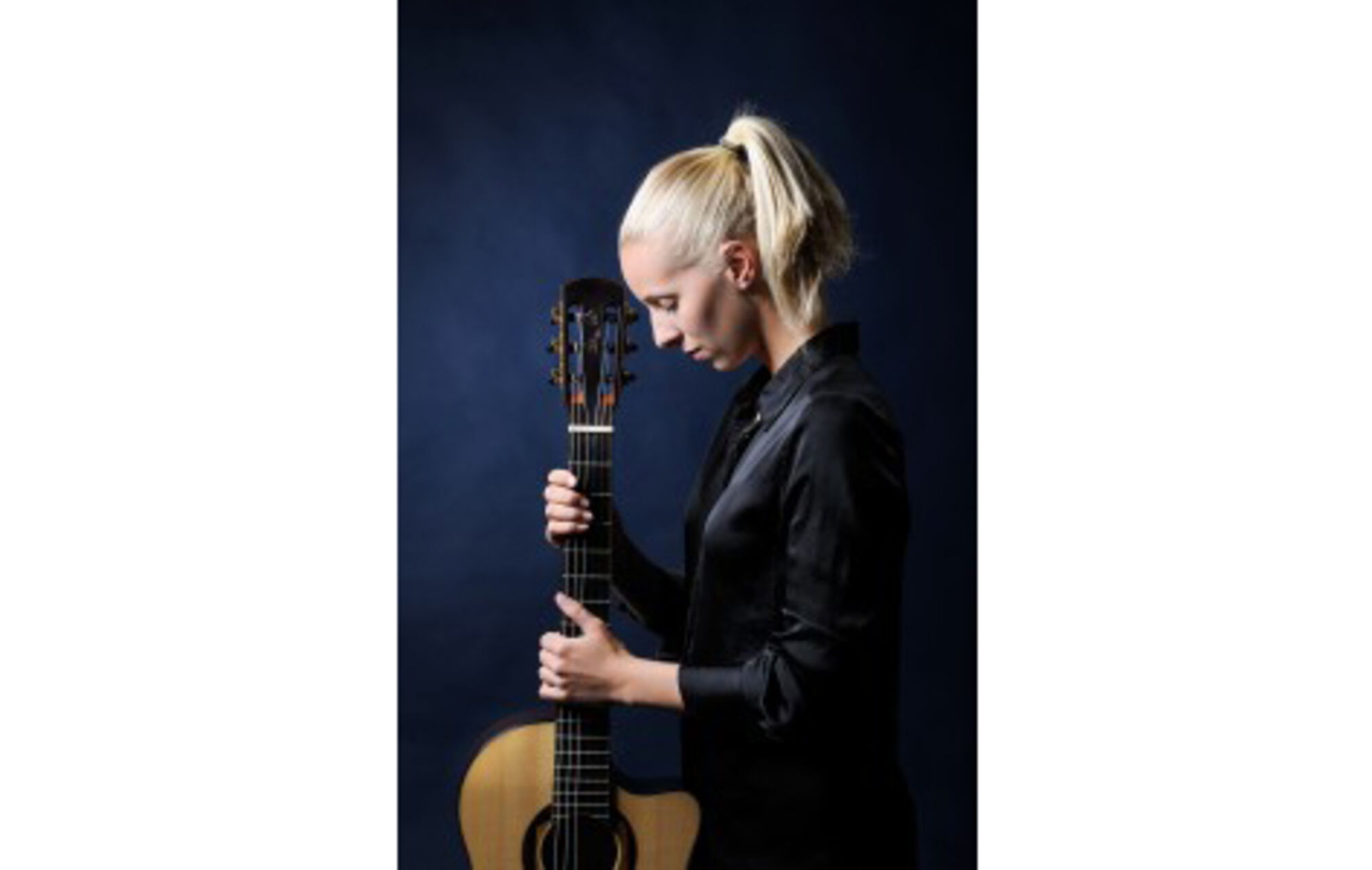 Musikerin aus dem Profil. Sie ist in schwarz gekleidet und hält eine Gitarre.