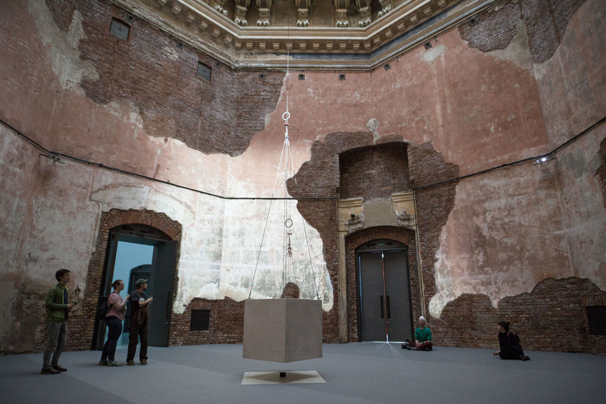Installation aus einem großen Würfel im Oktogon. Vier Personen schauen die Installation an.