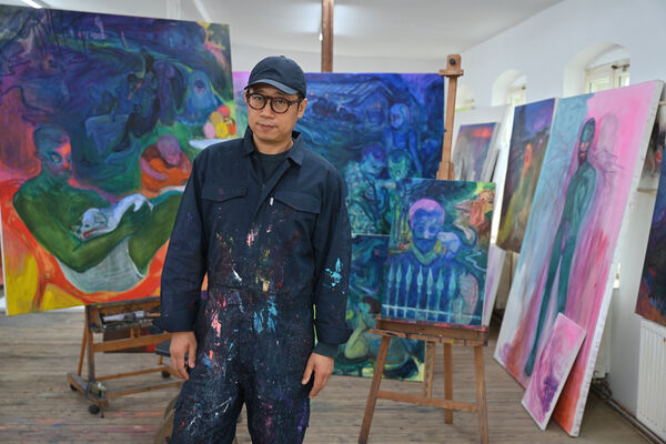 Rao Fu Painter Rao Fu in front of some colorful works of his