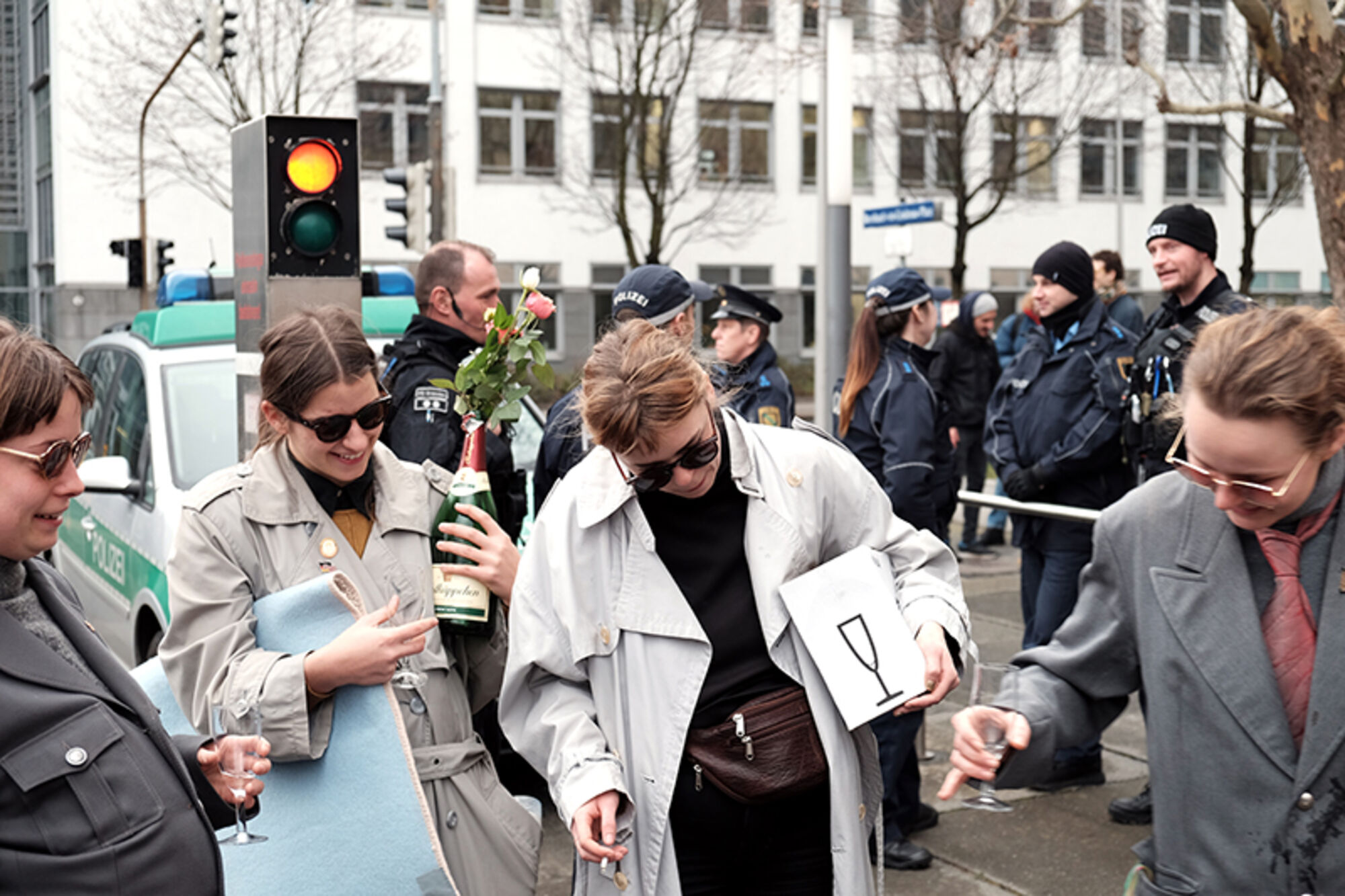 Frauen sind feierlich gekleidet und trinken Sekt auf der Straße. Polizisten im Hintergrund.