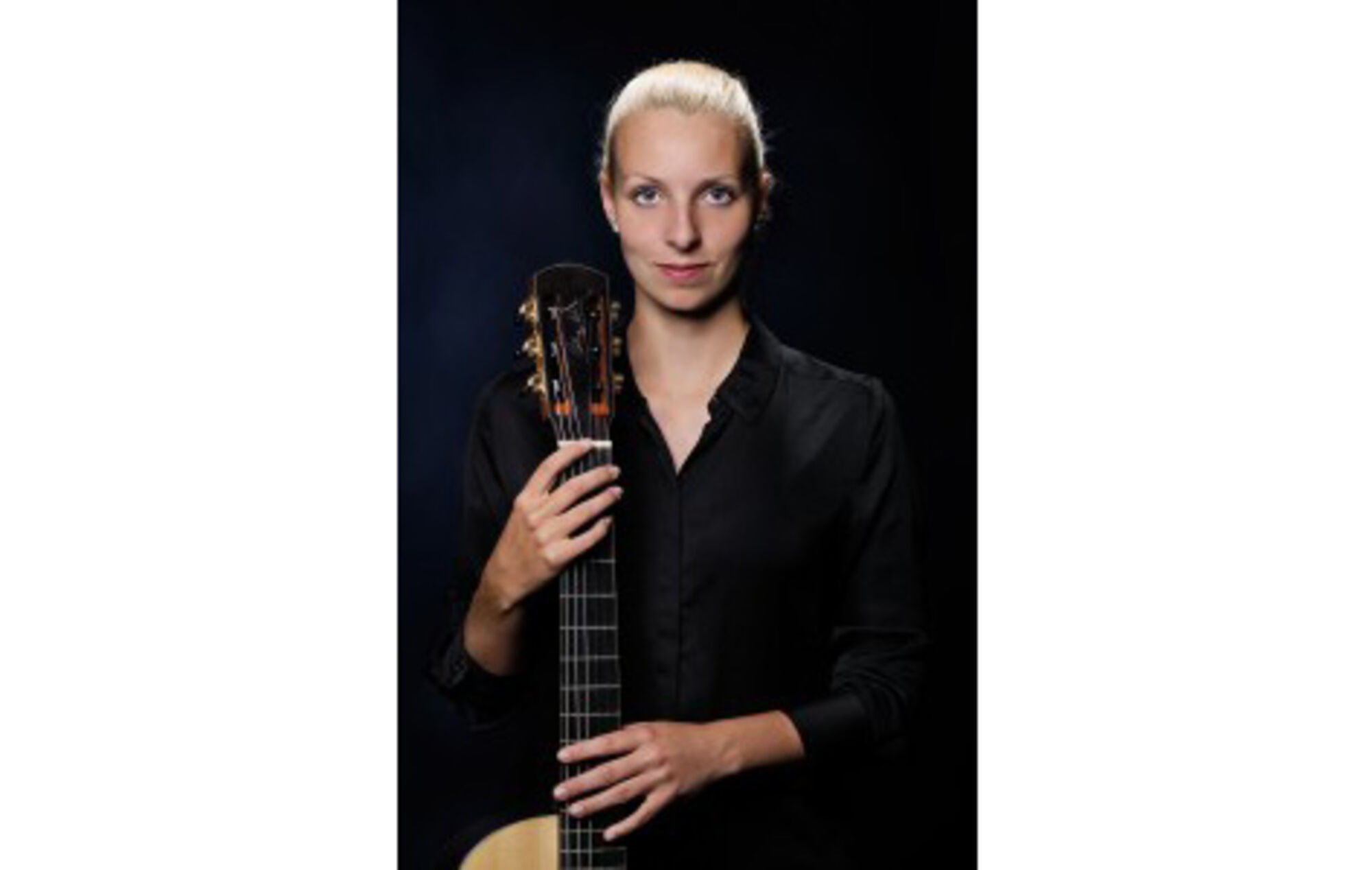 Musikerin, in schwarz gekleidet, hält eine Gitarre.