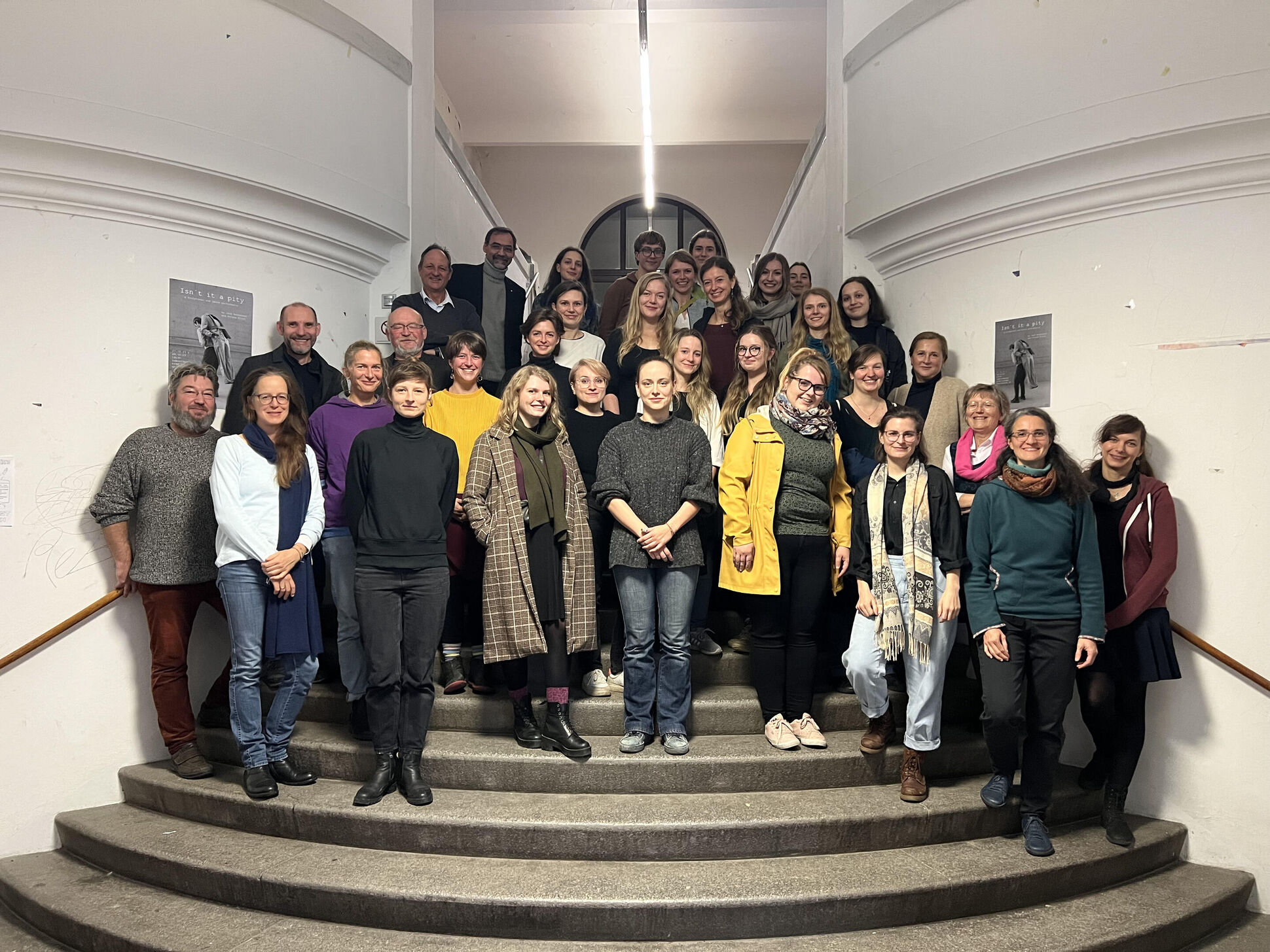 Gruppenfoto, weitwinkling aufgenommen, lächelnde Menschen stehen auf einer Treppe