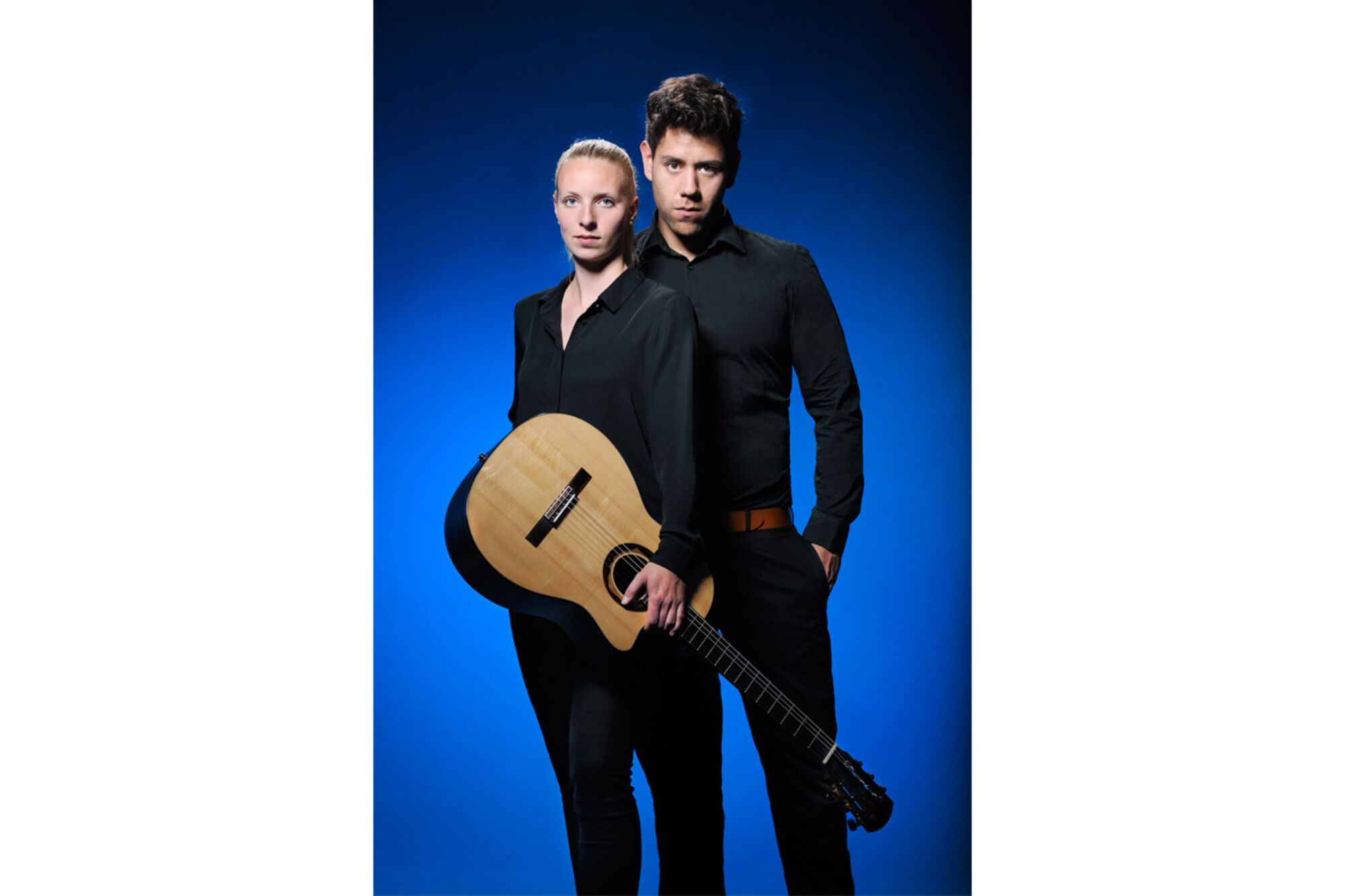 Ein Musiker und eine Musiker in schwarz gekleidet. Die Frau hält eine Gitarre.