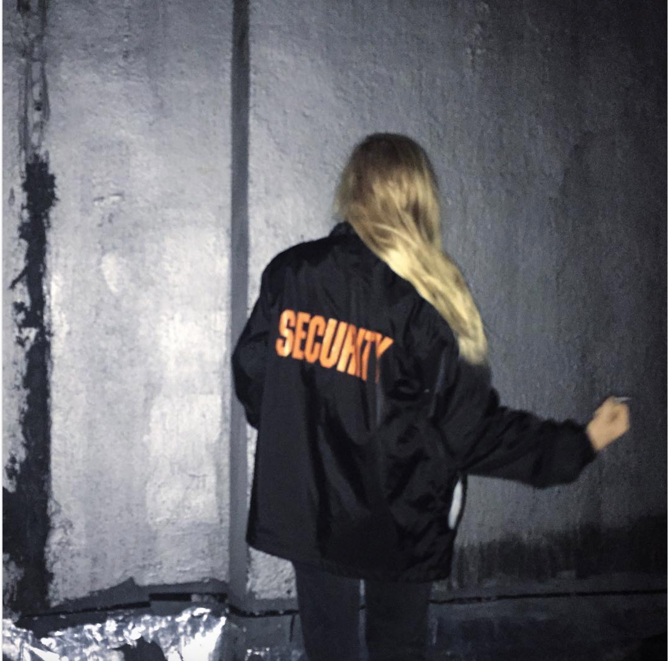Person mit langen blonden Haaren von hinten, Aufschrift des T-shirts: Security