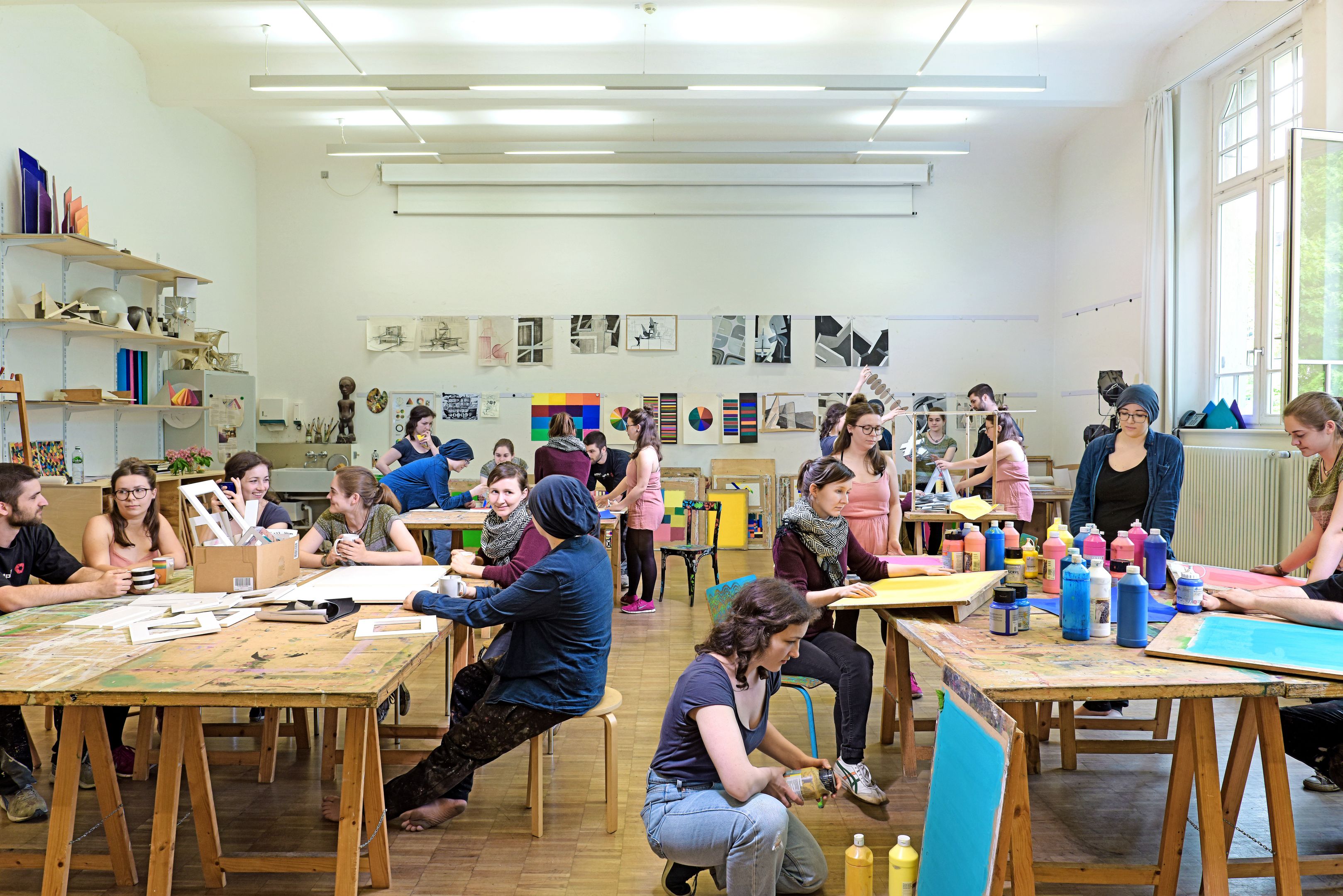 Atelier des Studienganges künstlerische Grundlagen. Tische, Stühle, Staffeleien und Farben im Raum. Bilder auf der Wand.