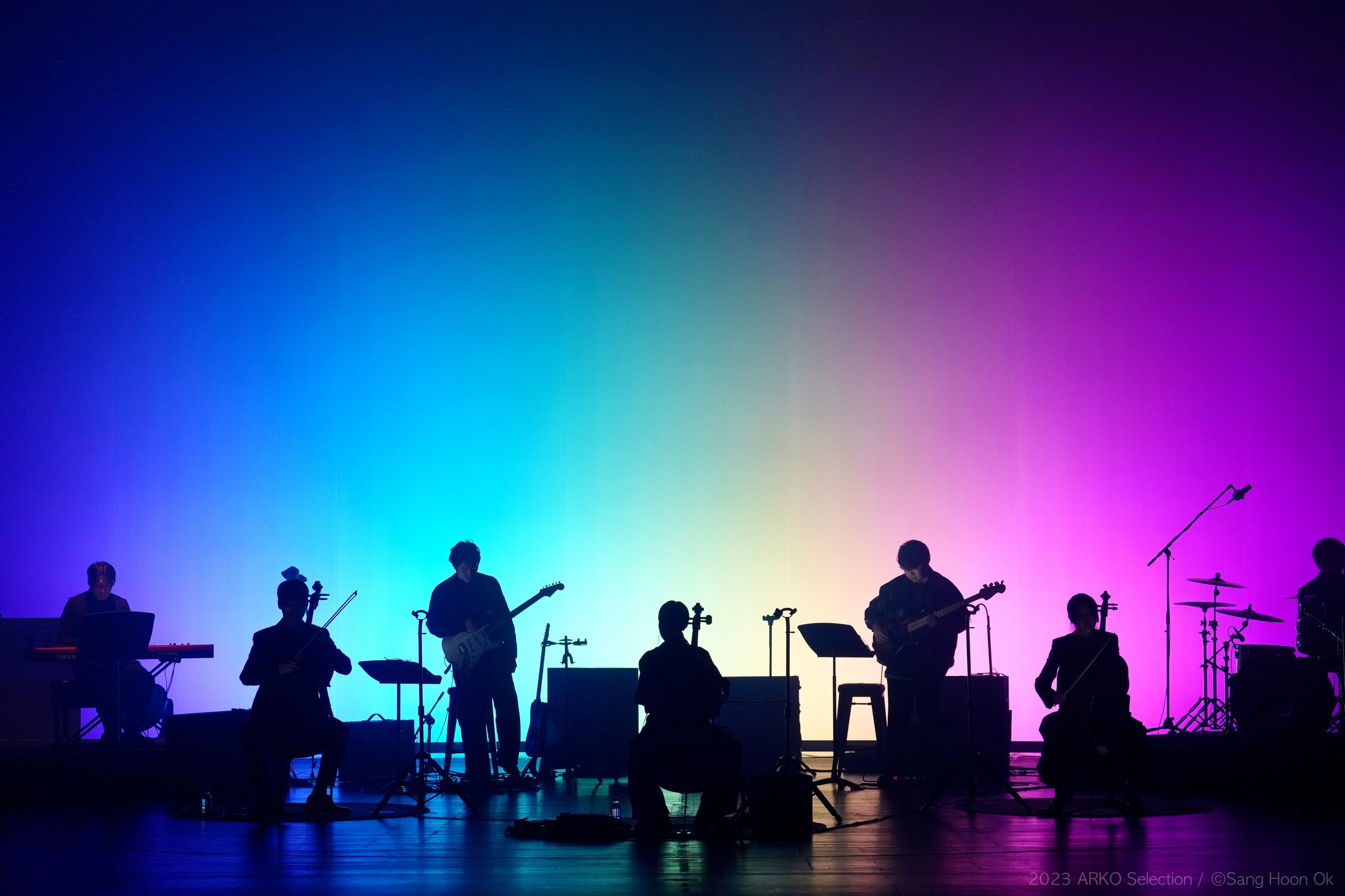 Silhouette of a band in front of a rainbow-coloured illuminated background