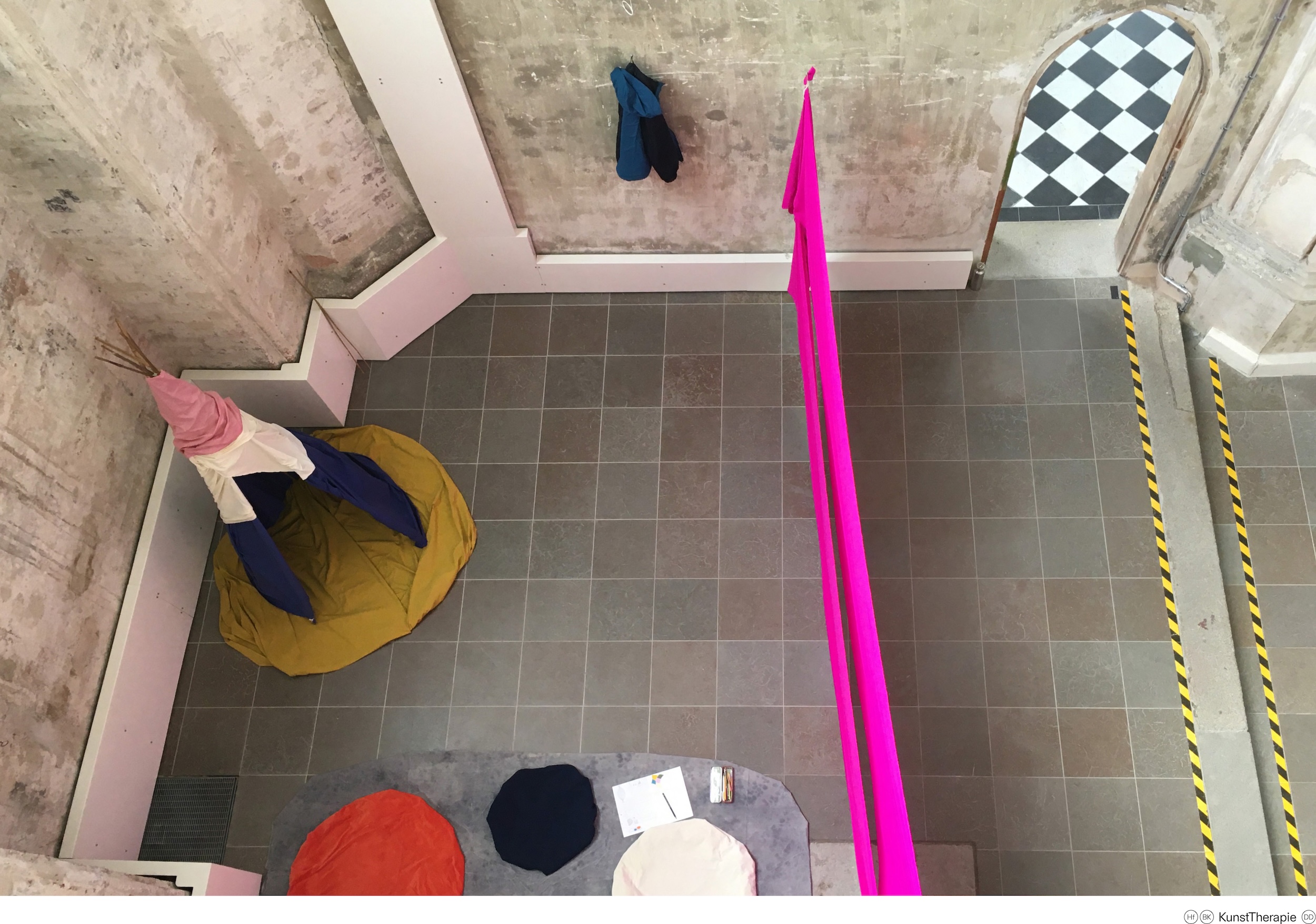 Draufsicht: Aufgespannter pinker Stoff, dahinter spitzes Zelt und Sitzflächen mit Textilien