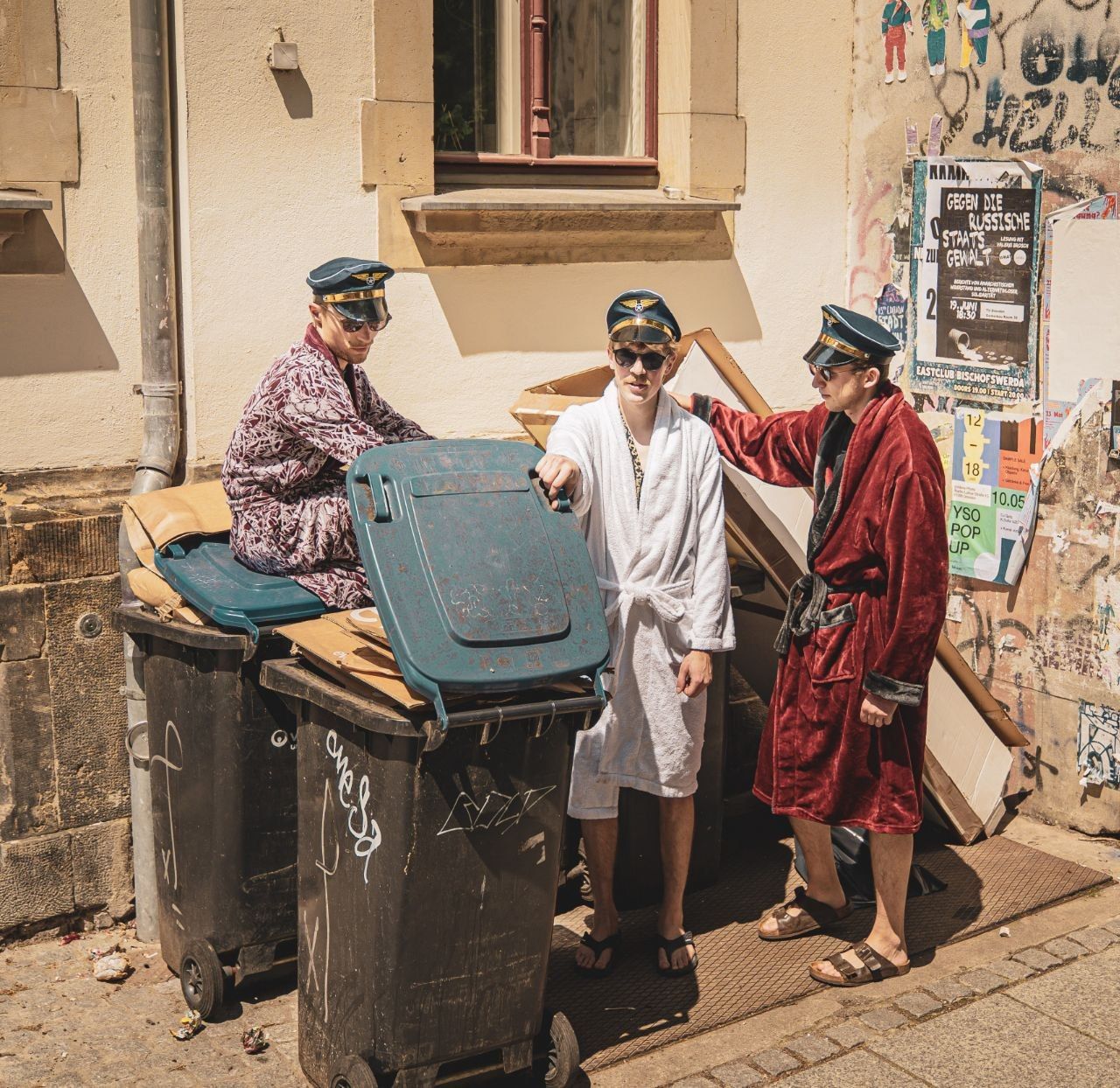 Bandfoto Kotpiloten. 3 Typen in Plüschbademänteln neben Mülltonnen